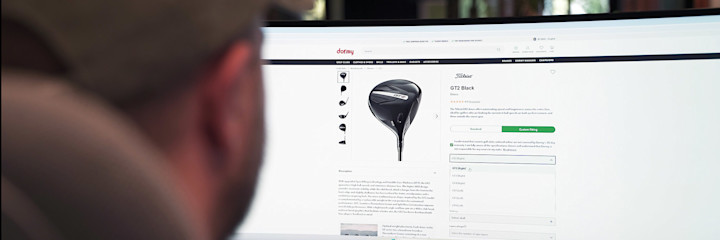 Person tittar på en datorskärm och bläddrar bland golfklubbor på Dormys webbshop, med en Titleist GT2 Black driver visad.