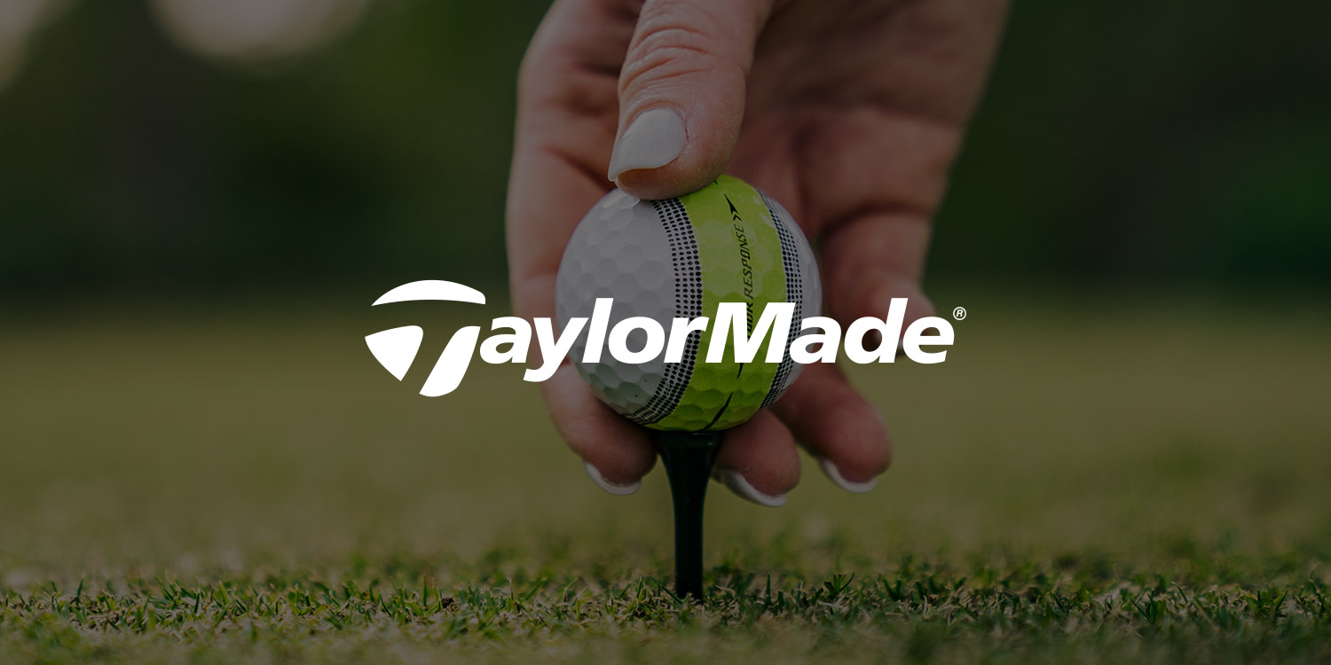 Logo: TaylorMade-text över en hand som placerar en golfboll på en peg på gräset.