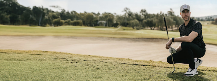 One carries a golf bag over their shoulder and walks outdoors on a golf course, dressed in a blue polo shirt and cap.