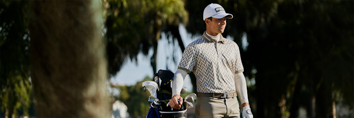 Man i vit keps och mörkblå pikétröja med mönster på ryggen tittar ner, texten "J.LINDEBERG" syns i vitt.