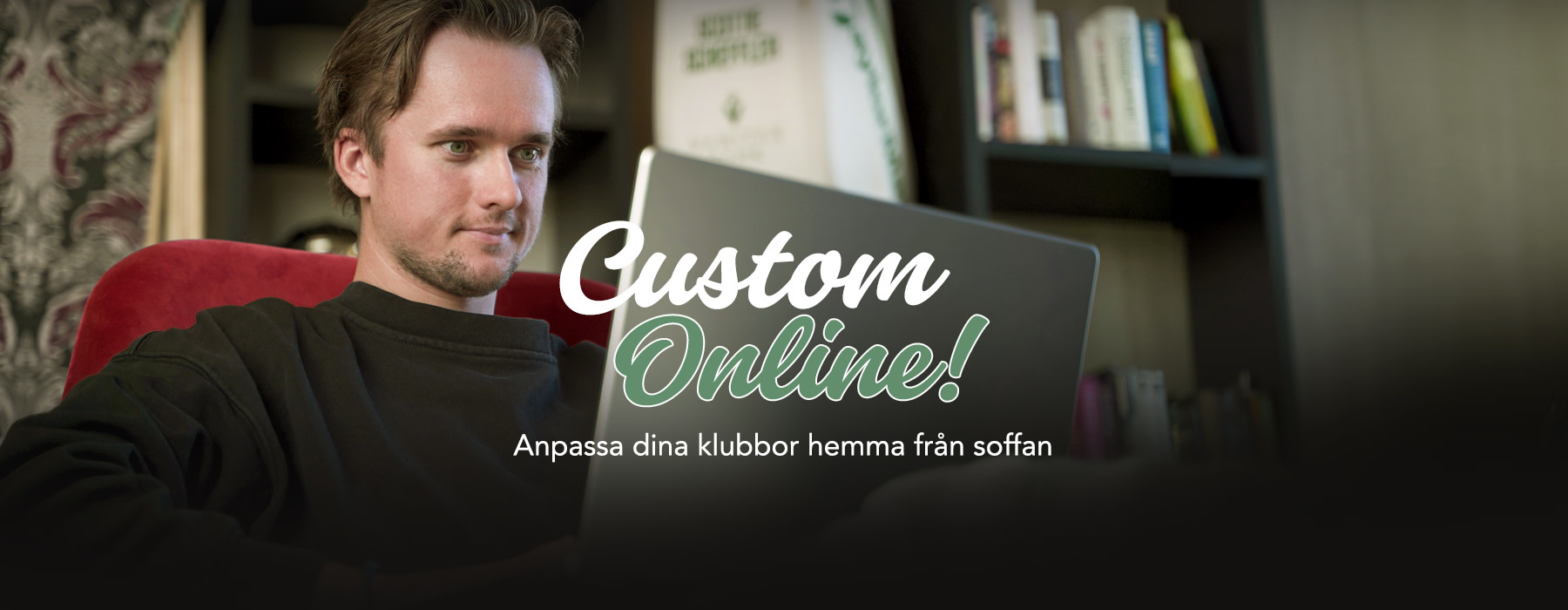 Man sitter i en röd stol och arbetar på en bärbar dator med texten "Custom Online!" över skärmen, bokhylla i bakgrunden.